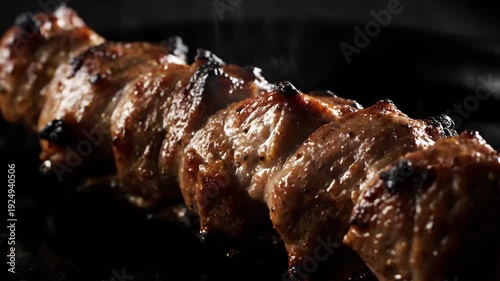 Appetizing close-up of juicy meat skewers grilling and sizzling on a hot plate. Delicious caramelized shish kebab or yakitori steaming with high contrast lighting on a dark background.