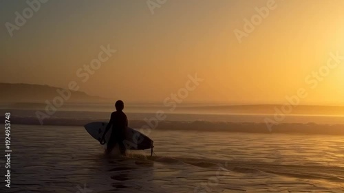 Surfer walking on beach at sunset with surfboard silhouette golden hour ocean waves.