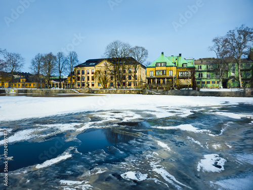 Fotografie Colorful Scandinavian Houses Reflected in Frozen River in Orebro, Sweden