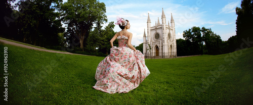 Princess in a vintage dress A woman wearing a floral dress is standing on a grassy lawn with a gothic church in the background.