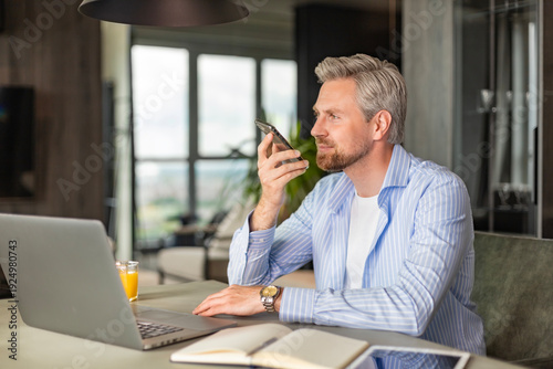 Photos Confident business man holding smartphone near mouth for recording voice message