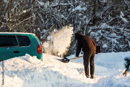 Man diligently shoveling heavy snow around his teal minivan after a winter storm. Clearing a path from the deep powder on a bright, crisp day. Balkan cyclone Francis in Central Russia, January 2026