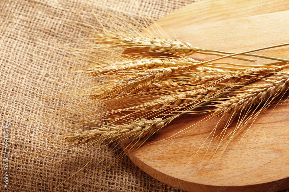 Naklejka premium Wheat ears placed on a wooden board on a burlap background in a farm setting