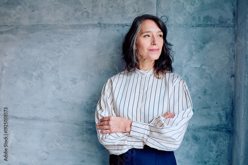 Quadro em tela Mature woman with gray hair crossing arms, looking away thoughtfully against a c