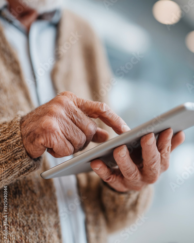 An older man is using a tablet to type on the screen. He is wearing a sweater and he is focused on the device