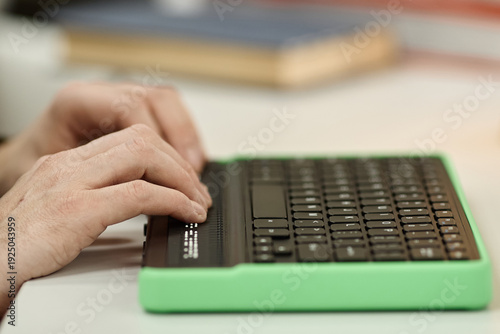 Caucasian adult man using braille display keyboard, hands reading tactile braille text in library setting, focusing on accessibility technology for visually impaired individuals