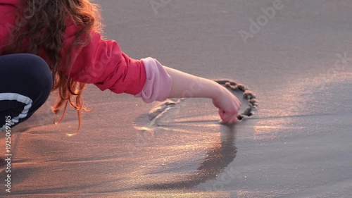 A girl draws a heart in the sand, which is then erased by the surf