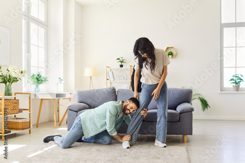 Couple quarrel, family problems and breakup at home, clingy man in despair and stress pleading with woman not to leave. Upset guy kneeling and clinging to partners leg, trying to stop girl leaving