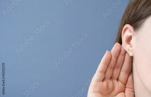 Woman listens attentively with her palm to her ear close-up on a blue background.