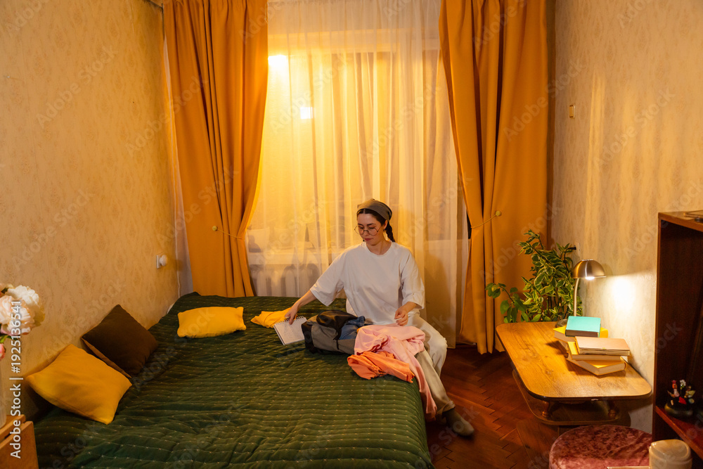 © _KUBE_ - Young Caucasian woman folding laundry indoors in evening light. She creates a tidy room. Home cleaning routine. Wide shot © _KUBE_ - Young Caucasian woman folding laundry indoors in evening light. She creates a tidy room. Home cleaning routine. Wide shot