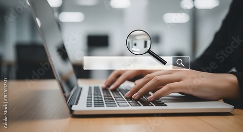 Businessperson's hands typing on silver laptop keyboard with illuminated search bar and magnifying glass icon in modern workspace