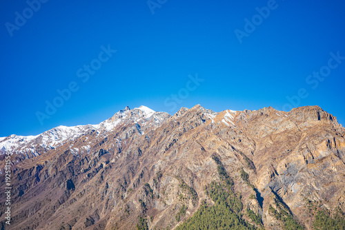 Foto Wide panoramic view of a rugged alpine mountain range with scattered snow patches and steep rocky ridges beneath a vivid blue sky