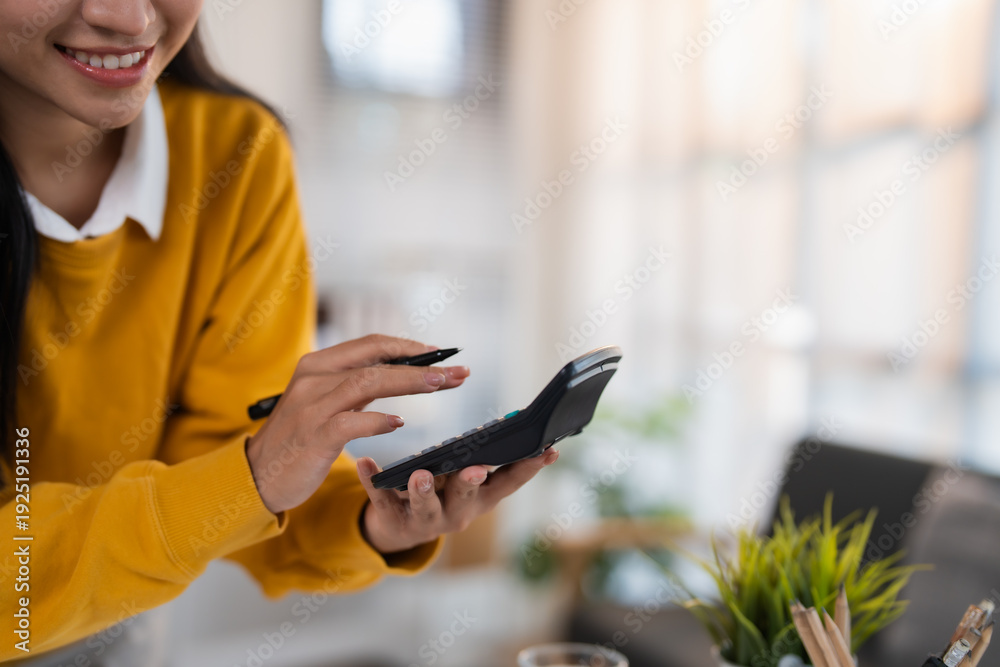 Fototapeta premium Smiling woman using a pen and calculator to review paperwork and manage personal and business finances, budgeting expenses, tracking income and planning savings confidently