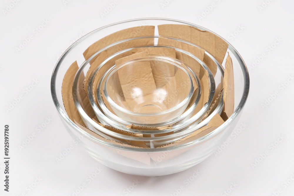 Four clear glass bowls of different sizes nested inside each other with protective brown cardboard spacers on a plain white background