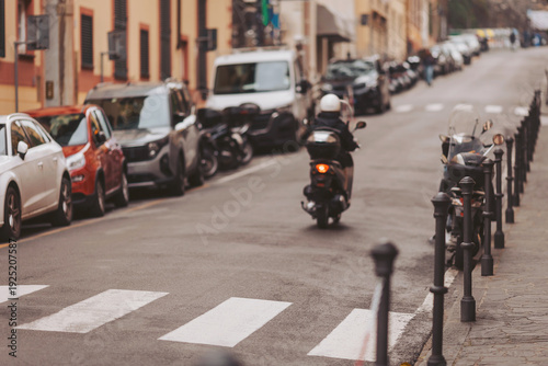 Wallpaper Mural A busy street showcases a scooter moving alongside rows of parked cars under a clear blue sky. Paved sidewalks and zebra crossings add to the lively scene Torontodigital.ca