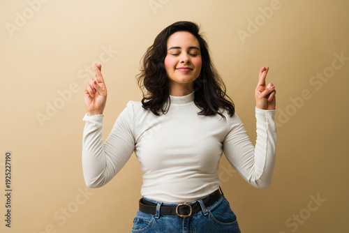 Fotografie Latin woman crossing fingers with eyes closed, wishing for good luck and success