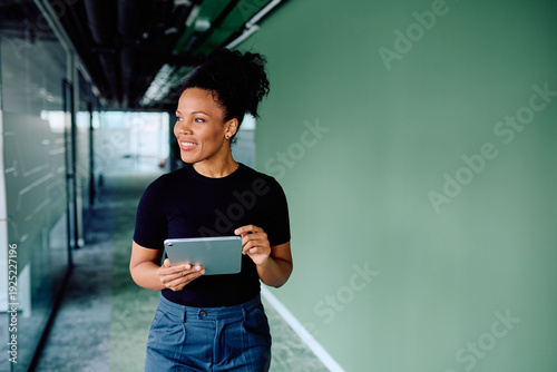Fotografie Professional black woman smiling, walking through a modern office corridor, and