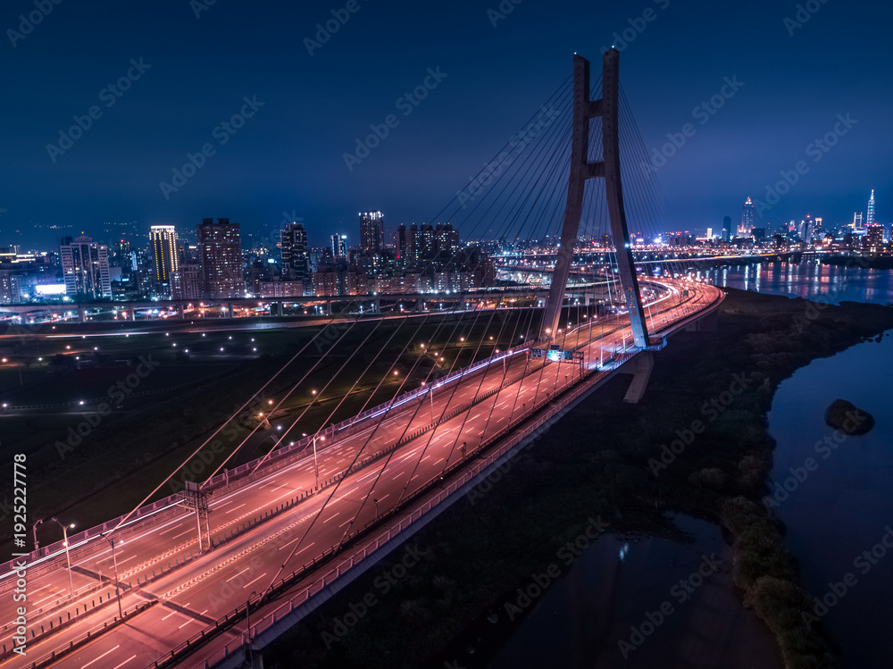 Fototapeta premium Car Light Trails of New Taipei Bridge - Long exposure of aerial photography use the drone at night in New Taipei, Taiwan.