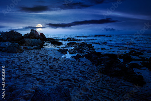 sandy beach landscape at night. full moon over coastal seascape scenery. mysterious nature background for summer vacation at the shore of black sea with rocks