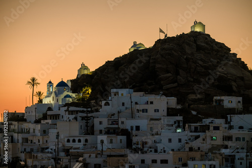 Panoramic view of the beautiful whitewashed village also known as chora, in Ios Greece, and a spectacular orange sunset in the background