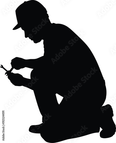 A crouching figure repairs something with a tool a striking silhouette