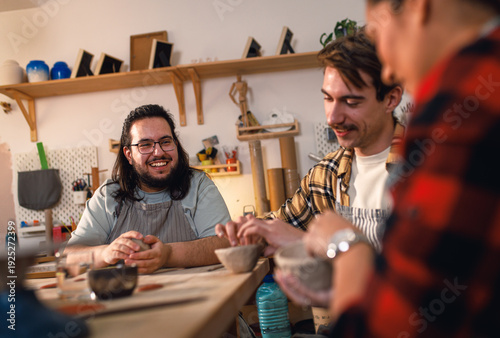 Man with his friends attending pottery class havng fun making clay objects together.