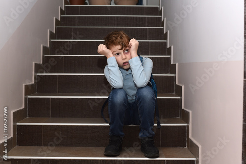 Sad schoolboy sitting alone on stairs with backpack, feeling stressed and upset at school, concept of childhood sadness, emotional stress and student mental health in education environment