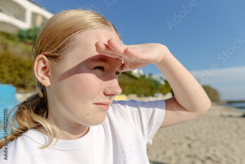 Photos Close up portrait of teen girl shielding eyes from bright sun while looking into distance on beach