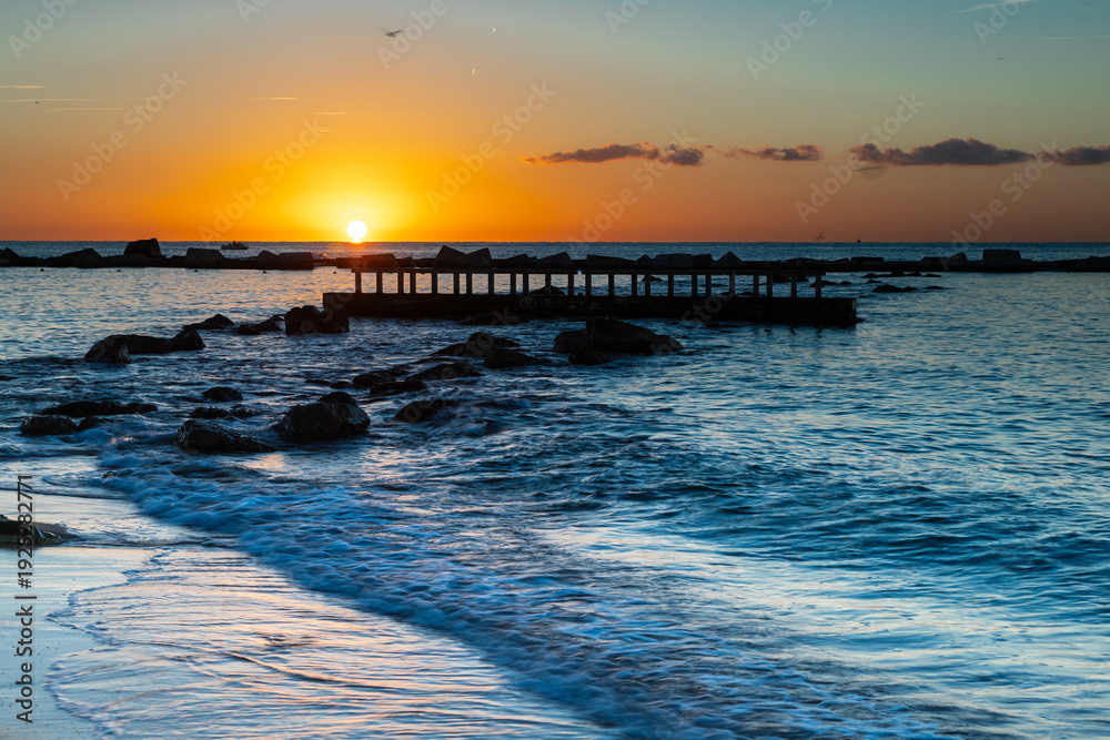 Naklejka premium Amazing colourful sunrise seen over the Mediterranean Sea from Barceloneta Beach, which is located next to Barcelona's classic fishing quarter. It is the cities oldest and best-loved beach and gives w