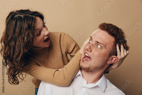 Foto Surprised man with red hair and freckles reacts to playful woman grabbing his head