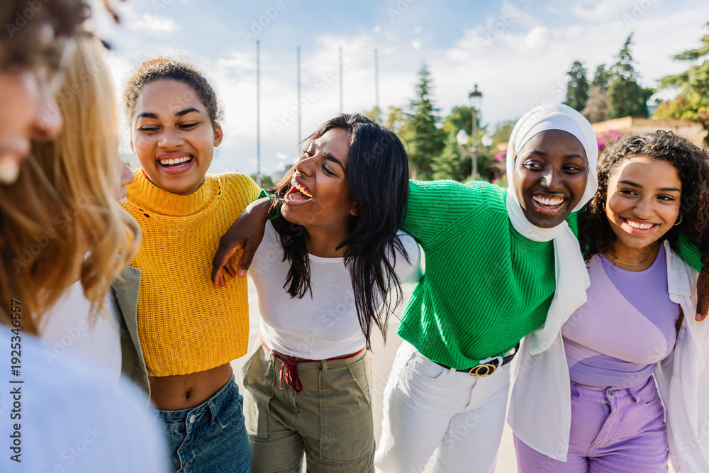 Fototapeta premium Group of diverse young women enjoying friendship outdoors. Smiling female friends spending time together in the city. Community and diversity concept.
