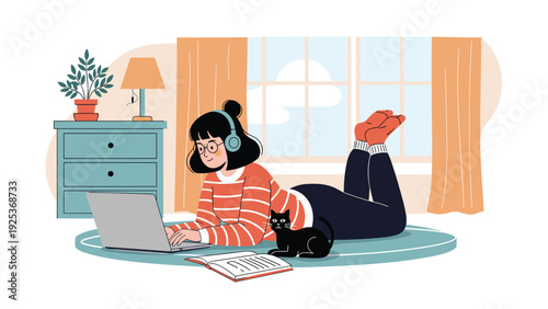Young girl wearing headphones lies on a rug while working on her laptop with a black cat and an open book by her side.