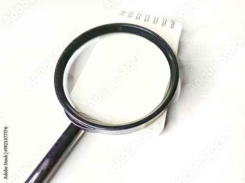 Magnifying glass and blank notebook on white background