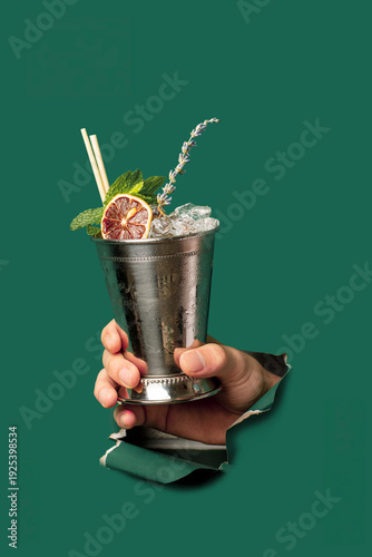 Tableau sur toile Hand Holding Metal Mint Julep Cup with Crushed Ice and Lavender through Green Pa