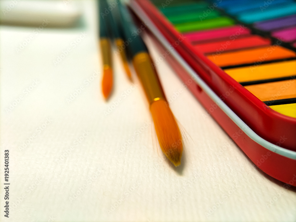 Fototapeta premium A watercolor set with vibrant colors is displayed on a white table. 