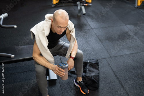 Athletic mature man with chocolate protein shake in modern fitness club after training session, recovery and sports nutrition concept.