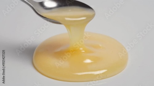 Spoon Lifting Thick Viscous Royal Jelly on White Background