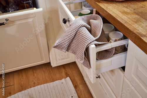 Open kitchen drawer with towel caught in it in messy modern interior. Unfinished household chores and everyday domestic routine concept