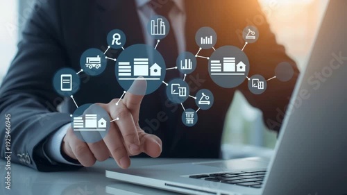 Person touching digital screen with icons for logistics, data, and business strategy near a laptop