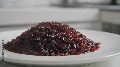A plate of red rice sits on a table with a blurred kitchen background, possibly for a recipe or food blog
