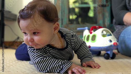 Billede på lærred Baby lying on floor, propped on forearms, vomiting with visible spit-up from mou