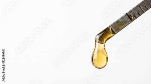 Wallpaper Mural A golden yellow viscous liquid drop hangs from a textured metal measuring tool against a clean white background Torontodigital.ca