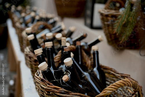 Wicker baskets with dark glass bottles on wooden shelf with light snow