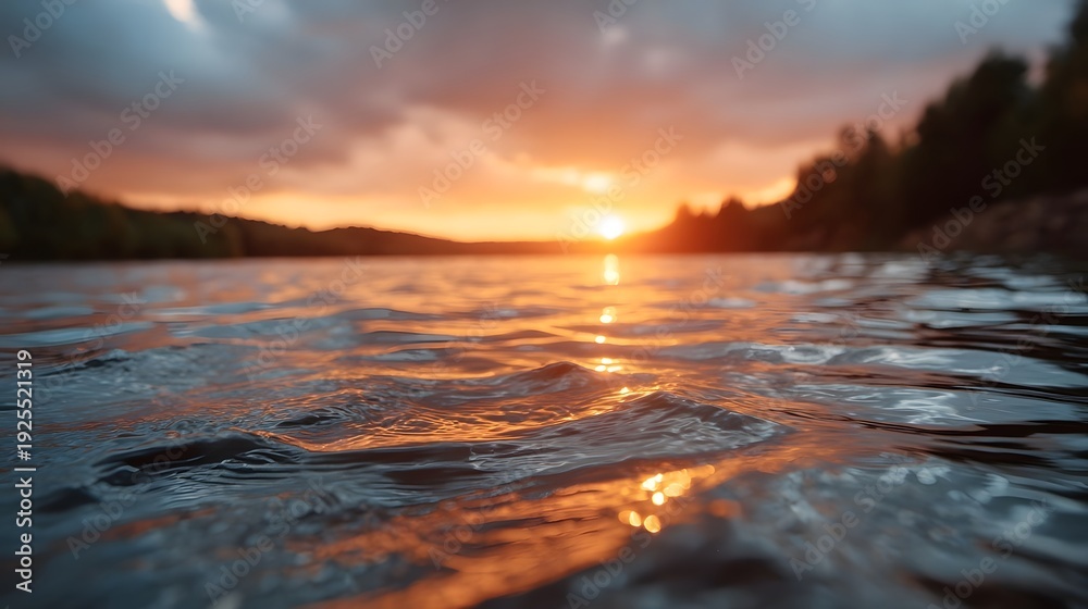 Obraz premium Golden hour sunset reflection on rippling water surface with blurred trees on the horizon at dusk