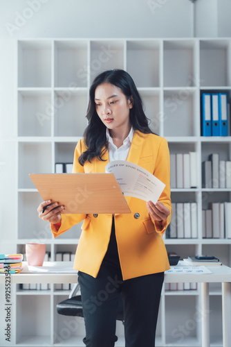 Focused Analysis: An astute businesswoman concentrates intently, meticulously examining documents within a modern office setting, showcasing diligence and professional insight.
