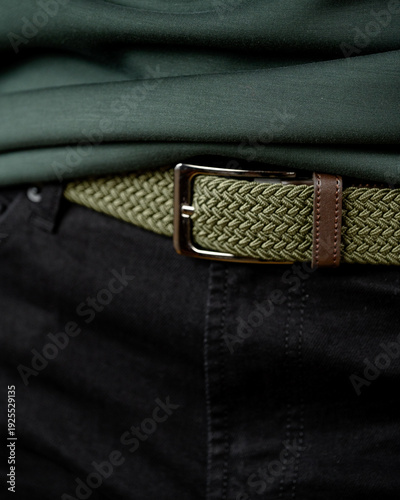 Green woven belt with brown leather accents worn over black pants