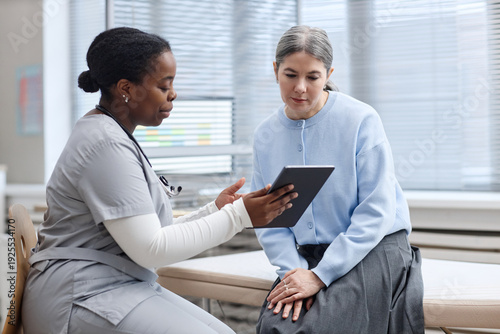 Foto Black young adult woman nurse showing digital tablet to Caucasian middle aged wo