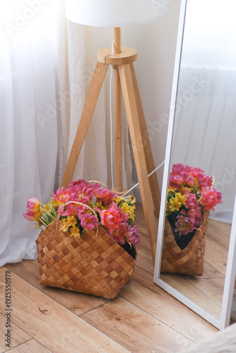 Woven basket with colorful flowers placed near a mirror in a cozy living room, home decor concept, spring decoration, natural interior style, springtime festivity.