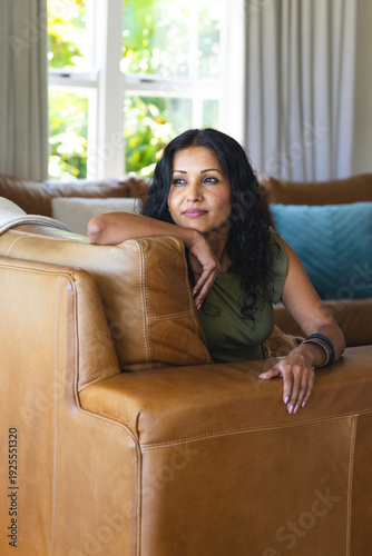Indian woman sitting on tan leather sectional sofa, wearing olive-green top and bracelets at home