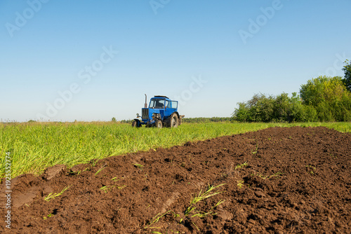 фотографія Blue tractor plowing a field under a clear blue sky on a sunny day